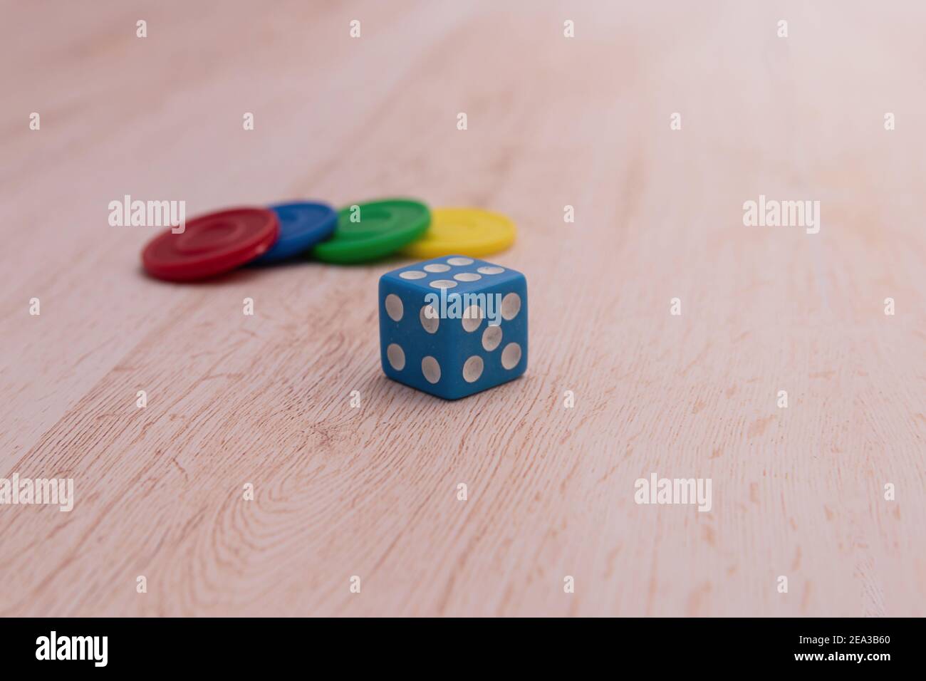 Chip di gioco colorati e un dado blu isolato su una superficie di legno. Concetto di giochi da tavolo e didattici. Il concetto di giochi da tavolo. Gioco da tavolo. Asse g Foto Stock