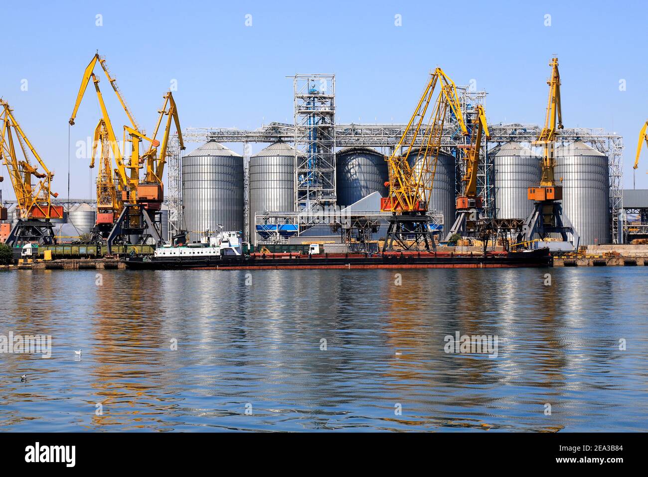 Grande porto in mare, porto, molo in riva al mare. Le gru gialle del porto scaricano una chiatta presso il porto marittimo di Odessa tra grandi serbatoi di metallo. Scarico delle navi Foto Stock