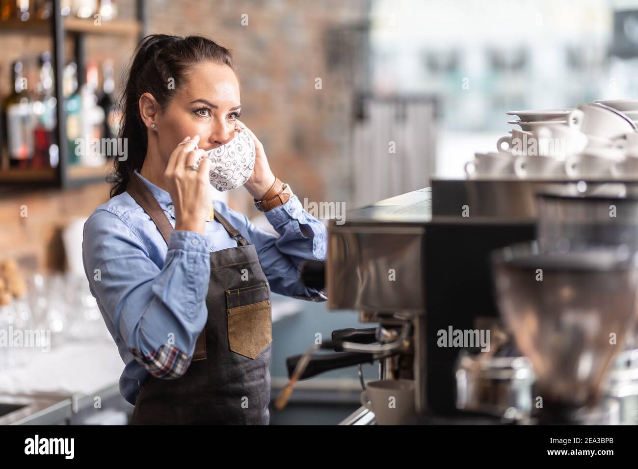 La cameriera mette su una maschera facciale in un caffè a causa delle misure adottate dal governo per limitare la diffusione del coronavirus. Foto Stock