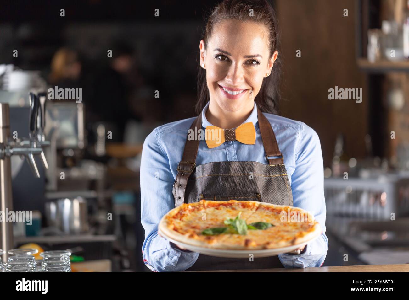 La cameriera sorride mentre serve una grande pizza italiana autentica in un ristorante. Foto Stock