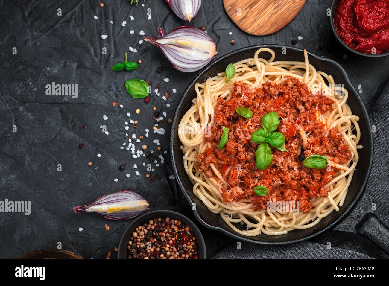 Fondo culinario con pasta e salsa di pomodoro ed erbe fresche su fondo nero di cemento. Foto Stock