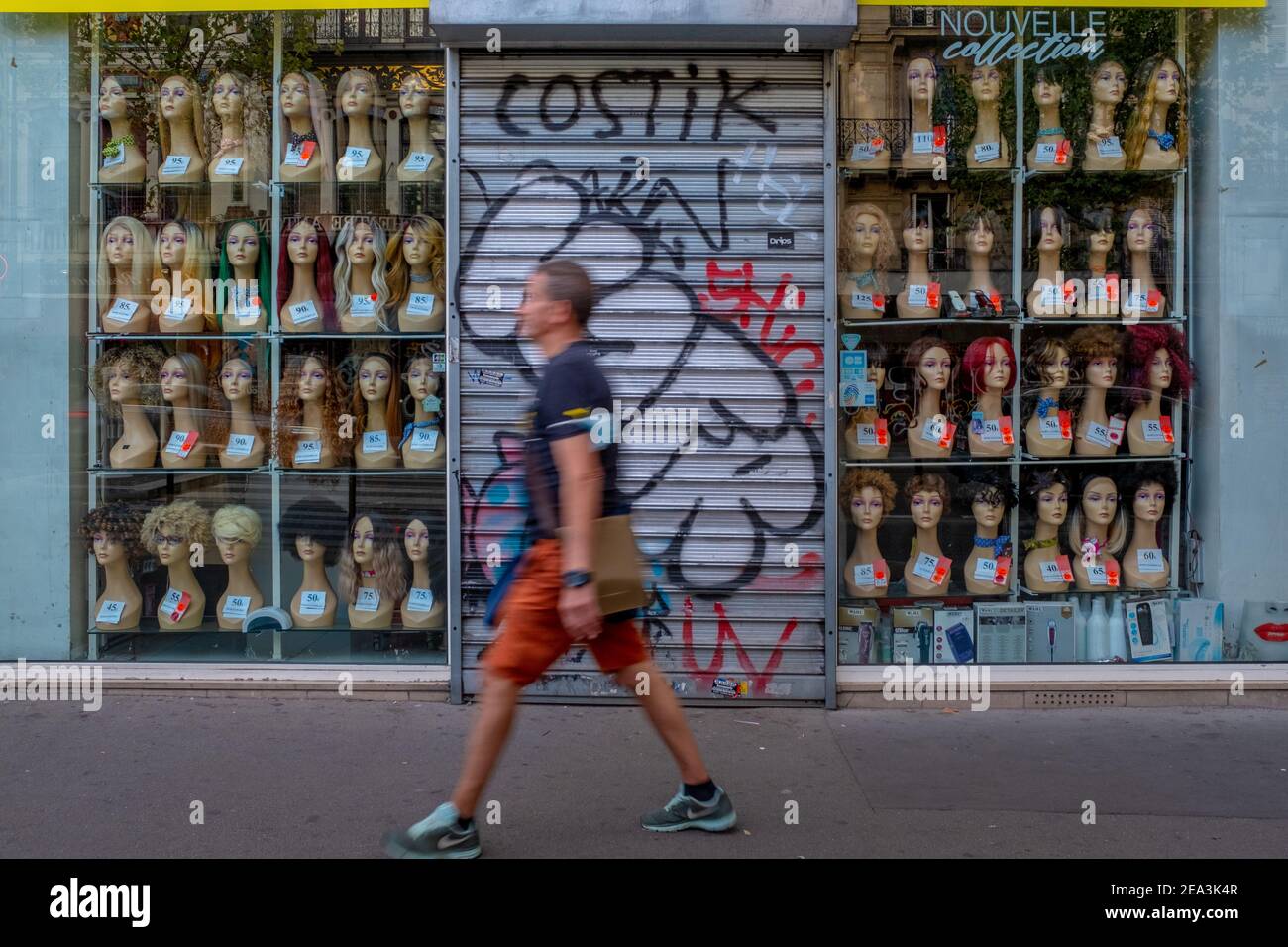 Il movimento offuscava l'uomo irriconoscibile che passava davanti a una vetrina in cui vi è una grande quantità di teste fittizie Mostra parrucche a Parigi Foto Stock