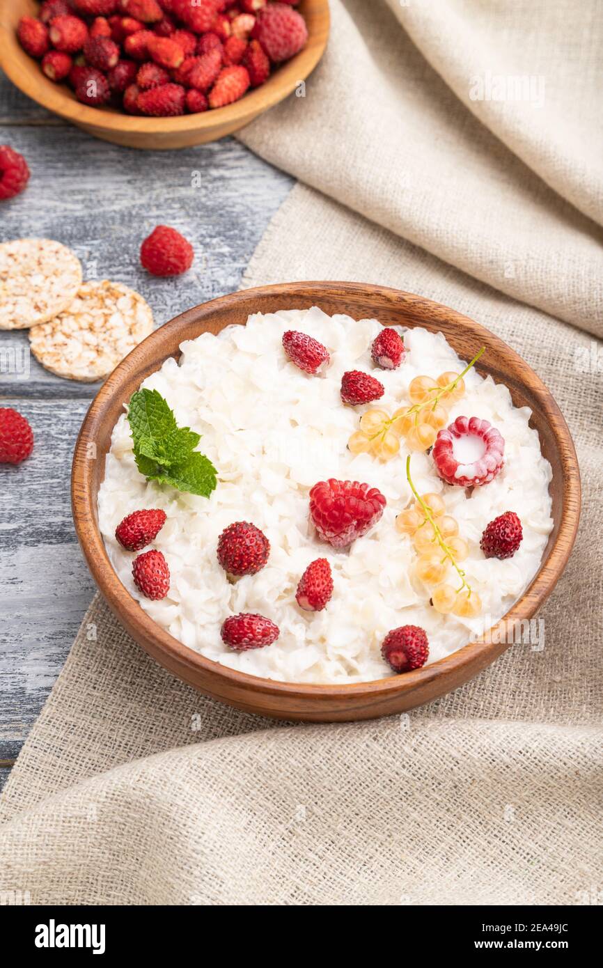 Riso fiocchi di porridge con latte e fragola in ciotola di legno su fondo grigio di legno e tessuto di lino. Vista laterale, primo piano. Foto Stock