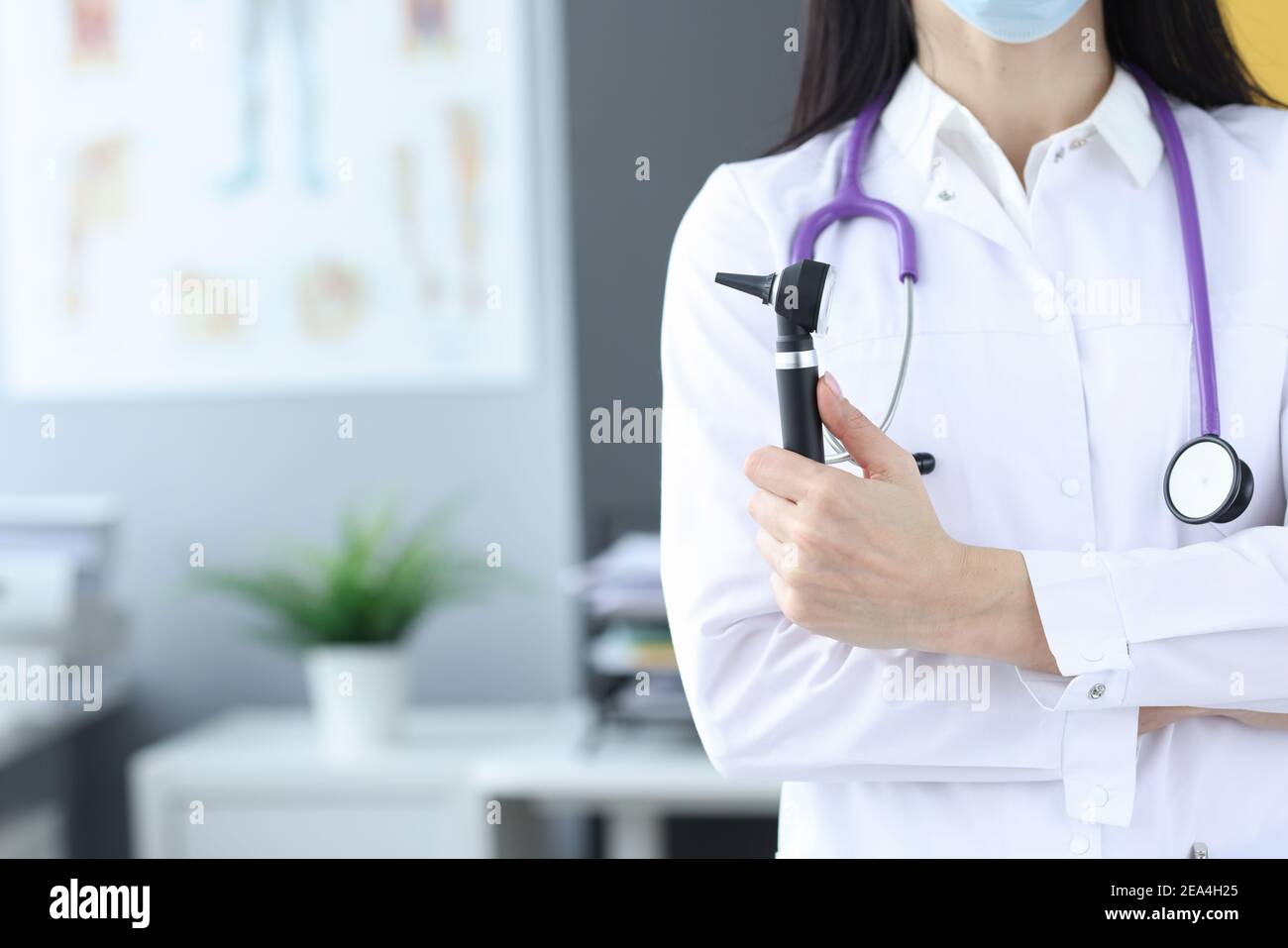 Medico in maschera protettiva tiene un otoscopio nelle mani Foto Stock
