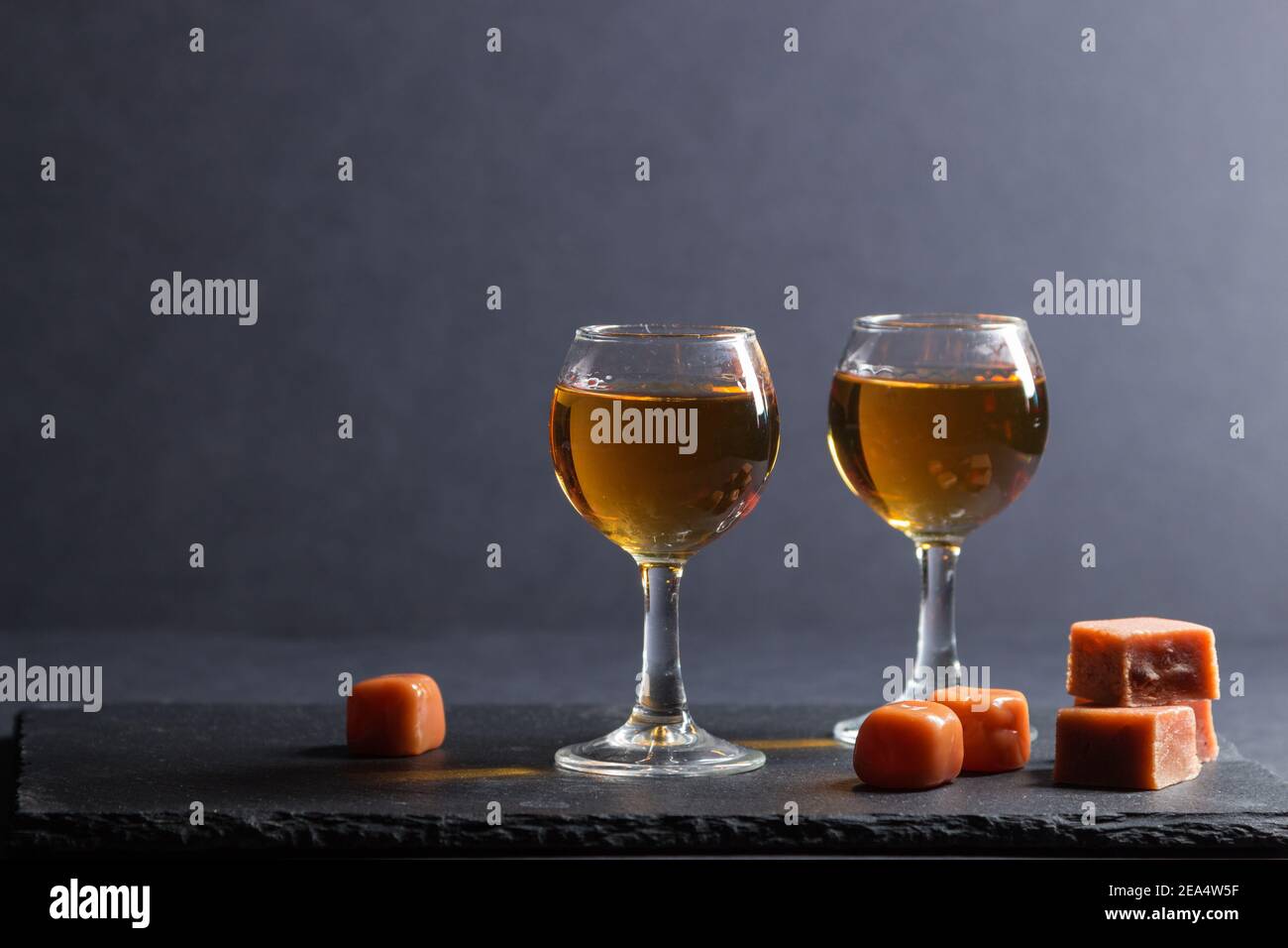 Bicchiere di whisky con caramelle al caramello su una tavola di ardesia di pietra nera su sfondo nero. Vista laterale, spazio di copia, messa a fuoco selettiva. Foto Stock
