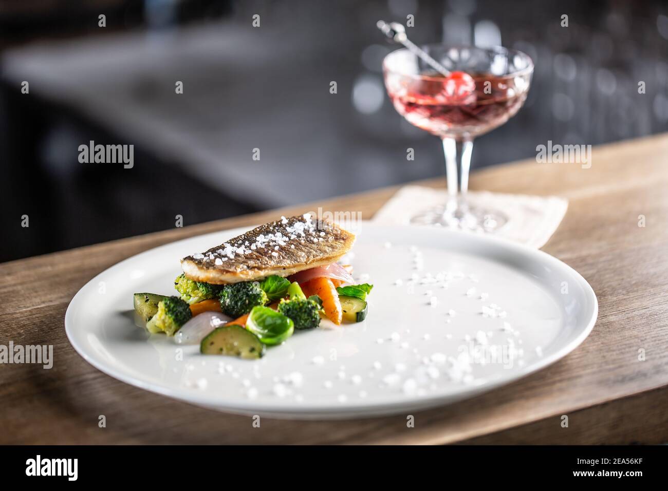Pesce sano cucinato con verdure al vapore servito su un piatto accanto ad un cocktail negroni. Foto Stock