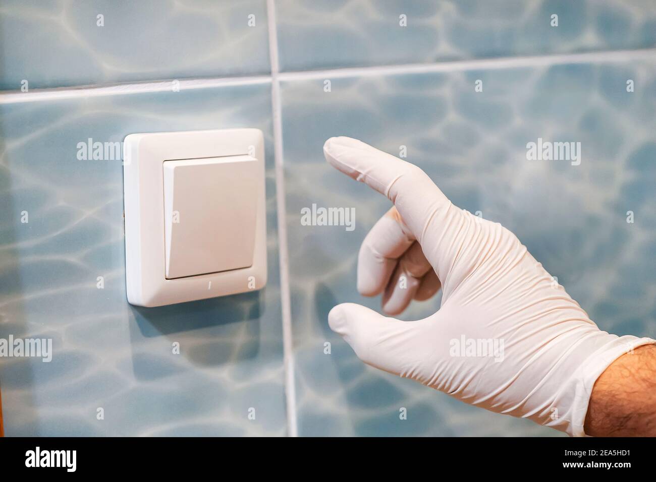 Una mano in un guanto di protezione bianco preme l'interruttore delle luci. Rischio di infezione da virus e batteri in luoghi pubblici. Igiene domestica. Foto Stock