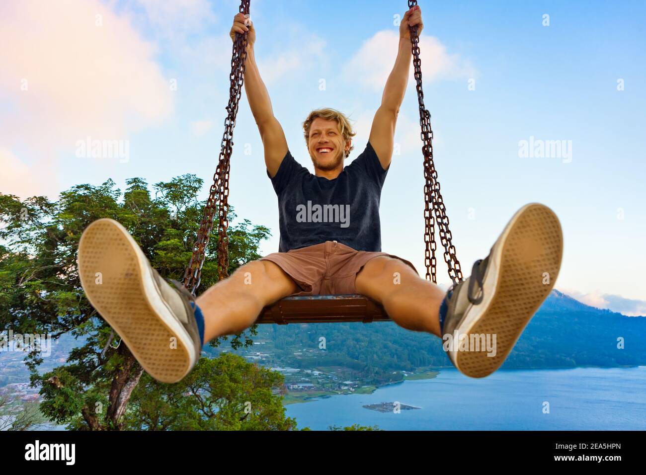 Vacanze estive. Il giovane si siede sull'altalena della corda dell'albero con la vista stupefacente della giungla. Altalena con divertimento sopra il lago tropicale. Buyan lago è popolare viaggio d Foto Stock