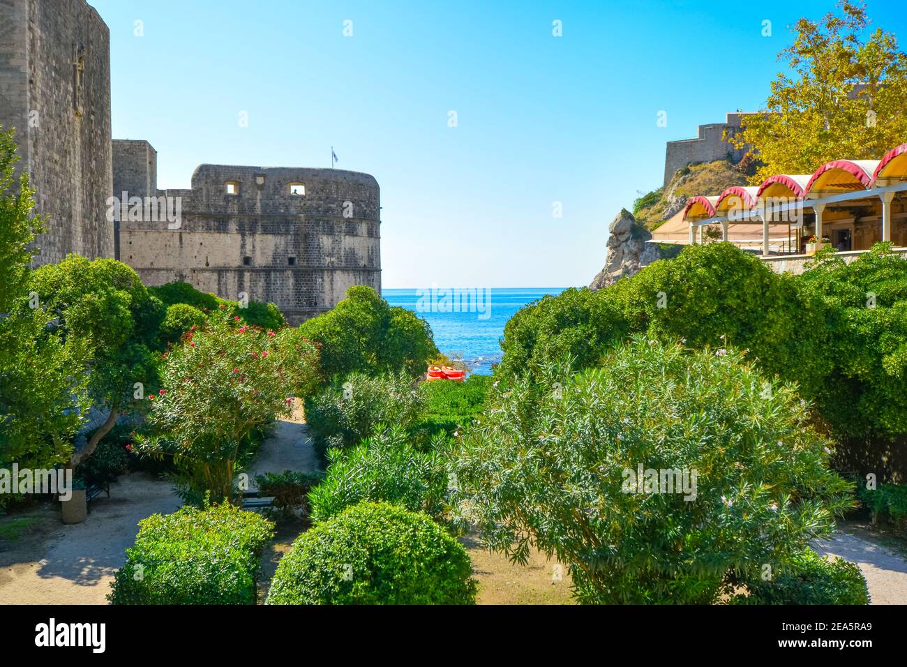 Vista delle mura della città medievale di Dubrovnik, Croazia, con l'Adriatico se vista dietro l'ingresso, con un piccolo parco sotto. Foto Stock