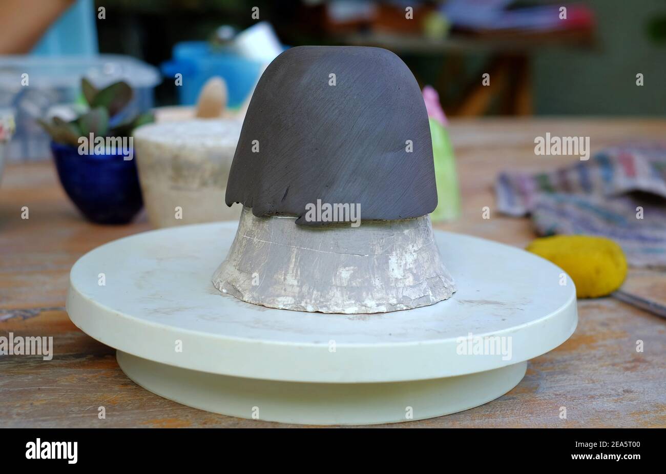 Un'immagine ravvicinata di un foglio di argilla che viene stampato in una tazza in uno studio di ceramica. Foto Stock