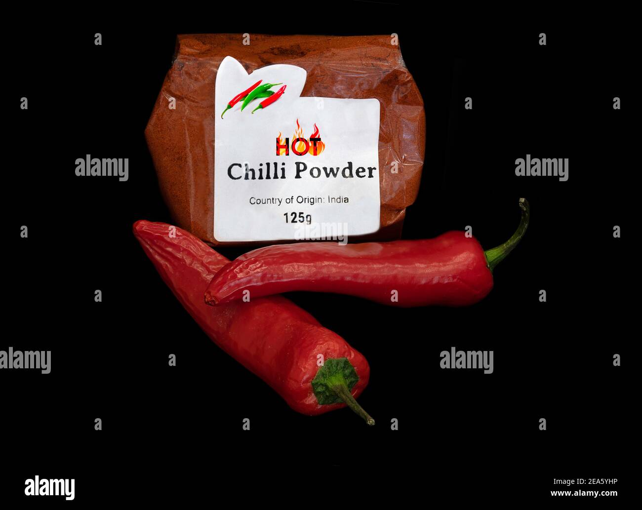 Su sfondo nero. Un sacchetto di peperoncino caldo in polvere con due peperoncini rossi freschi in primo piano Foto Stock