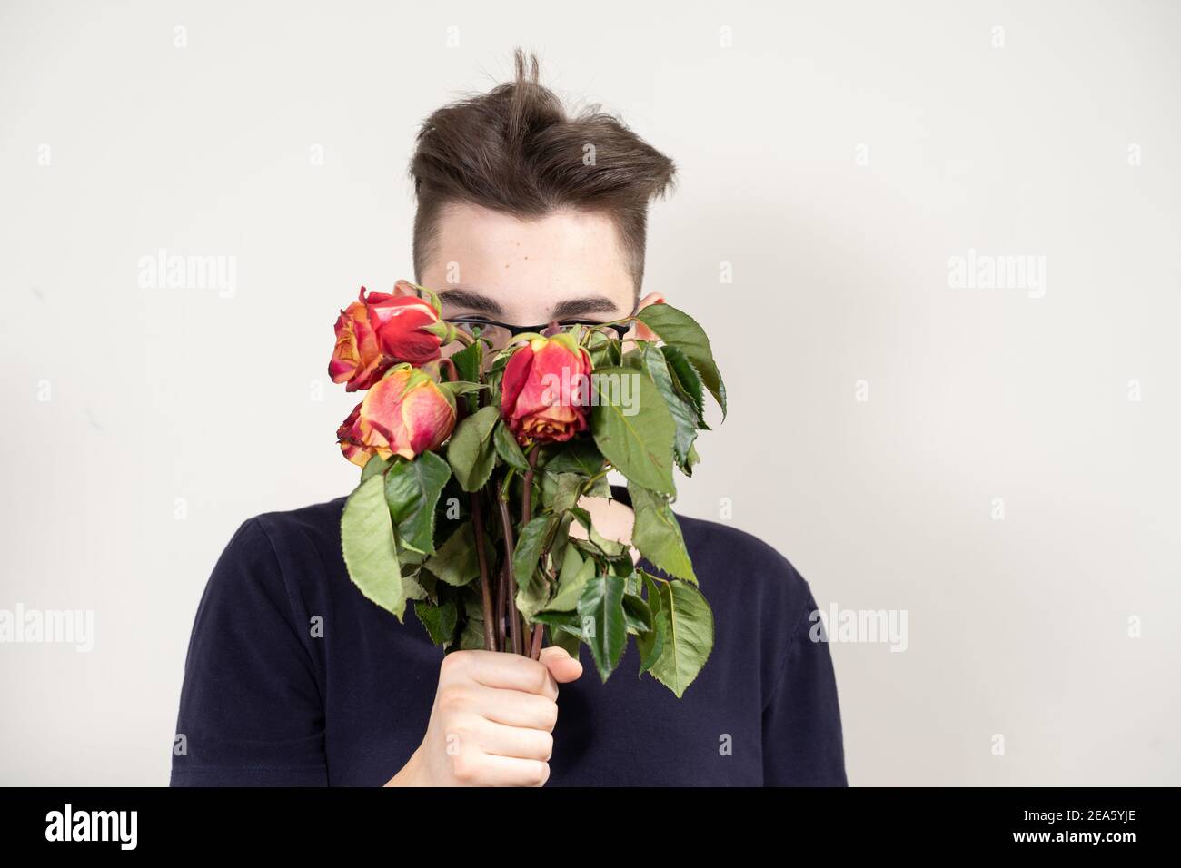 ragazzo in bicchieri con bouquet di rose rosse appassite. concetto di amore infelice Foto Stock