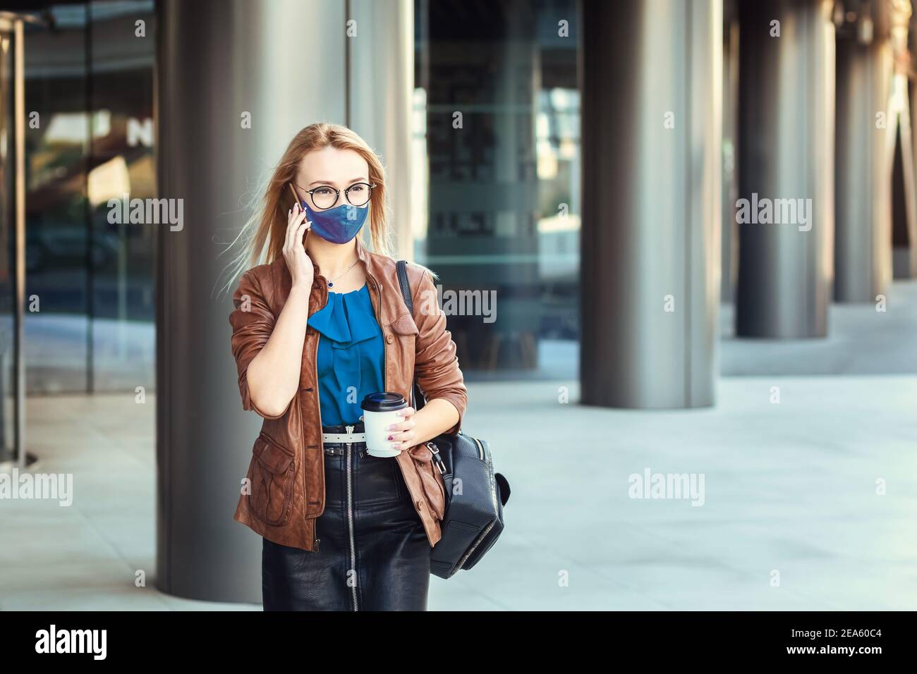 Donna che indossa una maschera che parla al telefono all'aperto mentre si è in viaggio Foto Stock