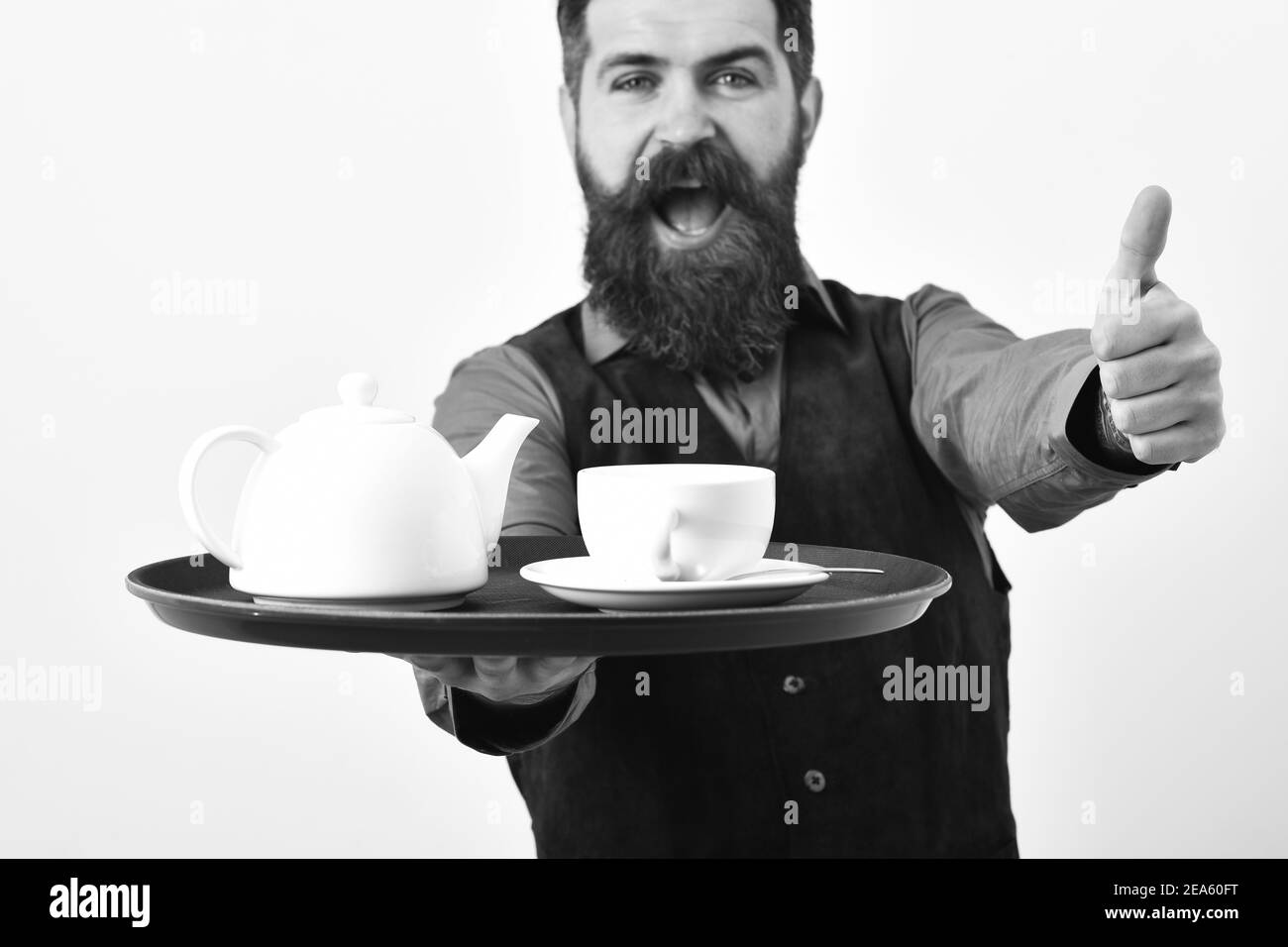 Cameriere con tisana bianca e pentola su vassoio. Concetto di ristorazione del ristorante. L'uomo con barba e baffi tiene il vassoio con piatti su sfondo bianco. Barman con faccia allegra serve tè mostrando super segno. Foto Stock