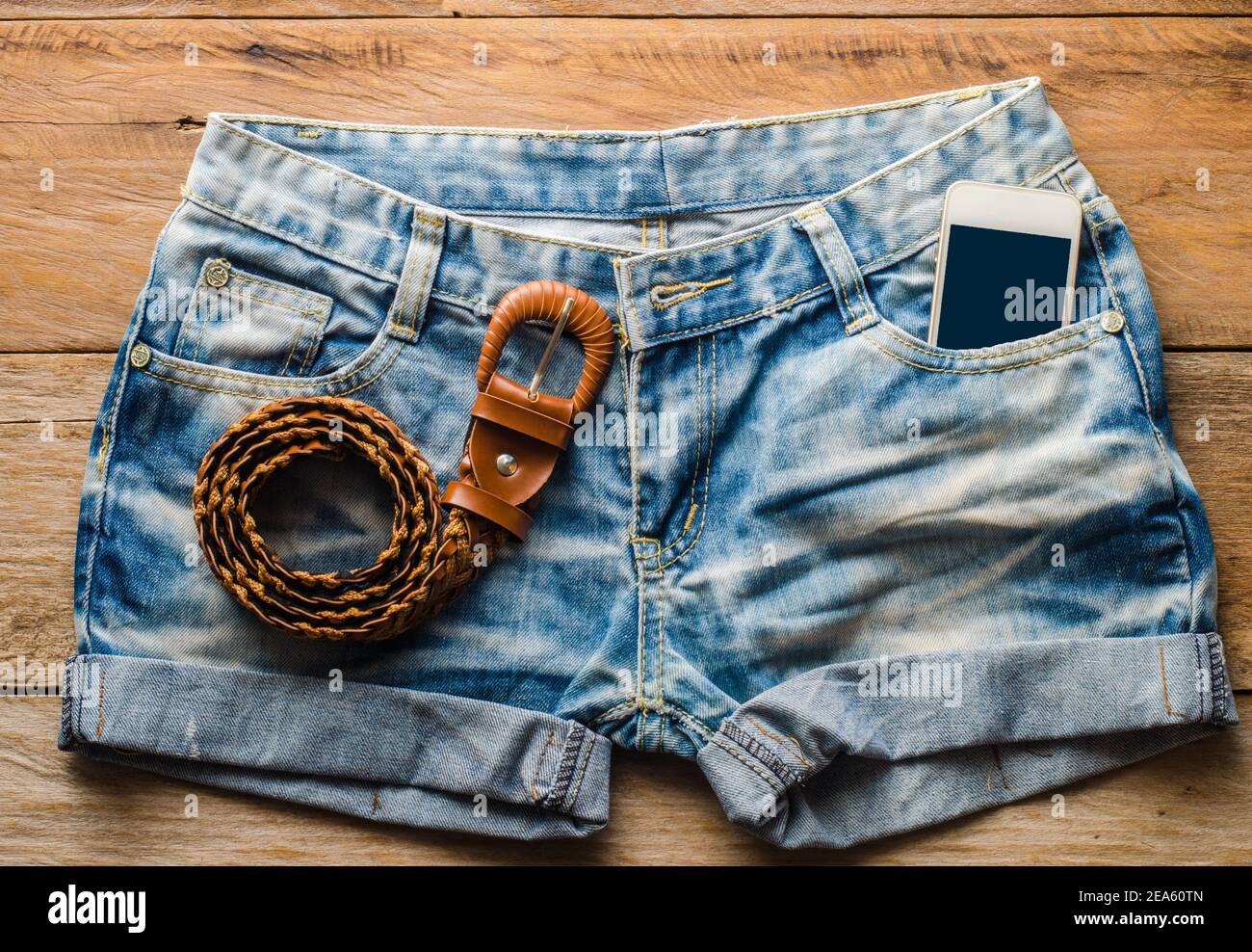 Pantaloncini jeans e smartphone sul pavimento in legno. Foto Stock