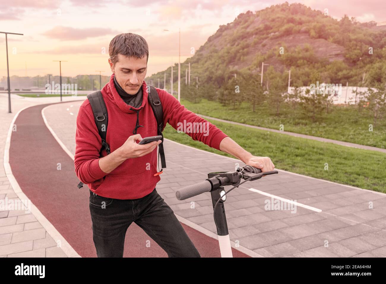 giovane uomo in libri di abbigliamento casual e paga per un condiviso scooter elettrico in affitto su una strada della città Foto Stock