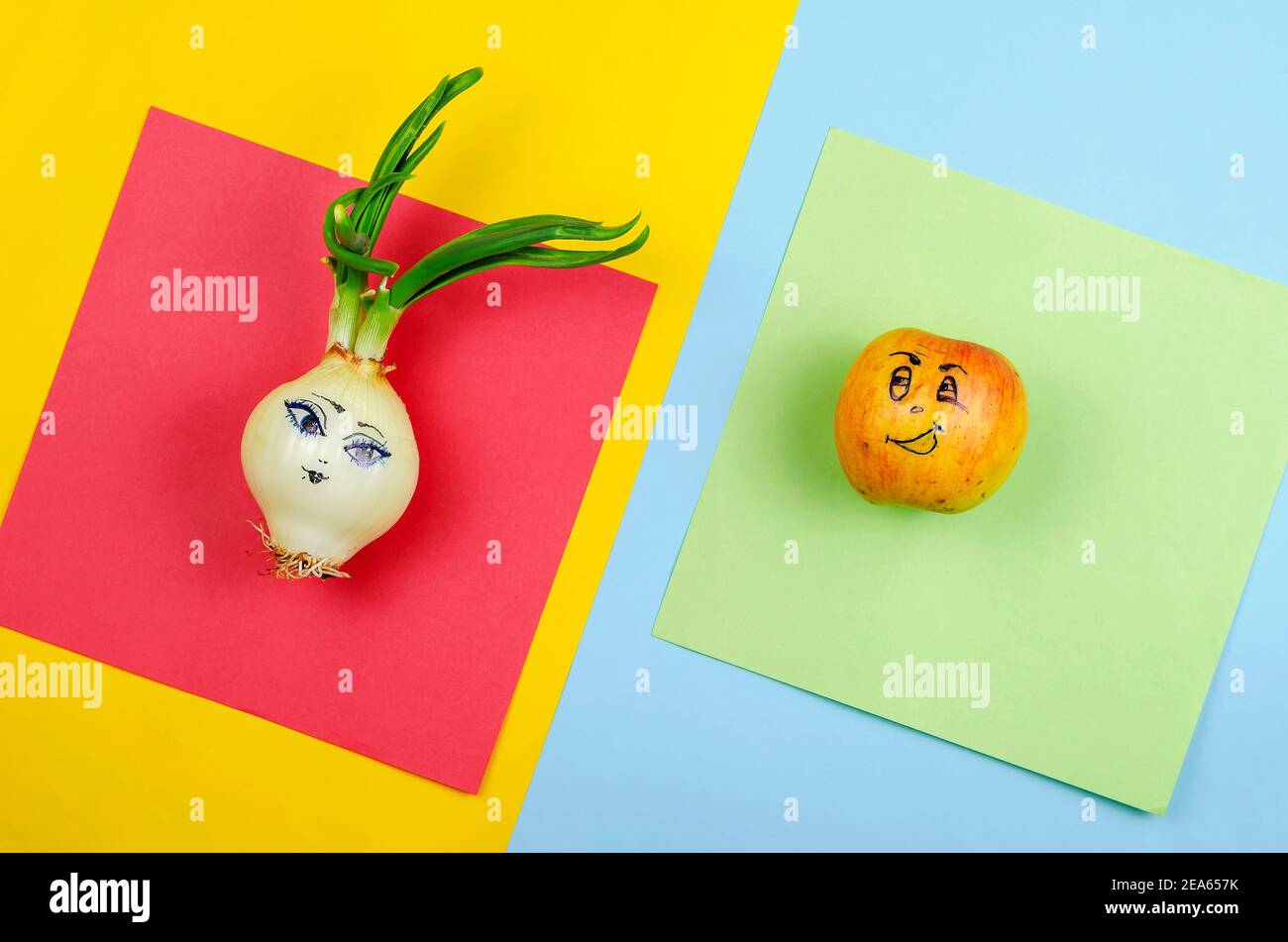 Composizione geometrica astratta con frutta e verdura. Una mela e una cipolla con facce dipinte su sfondo multicolore. Vista dall'alto, disposizione piatta Foto Stock
