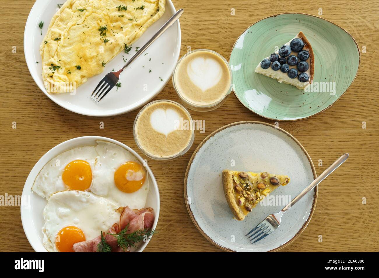 Colazione luminosa su sfondo di legno marrone, vista dall'alto. Dessert gustosi, omelette, uova fritte e tazza di caffè. Foto Stock