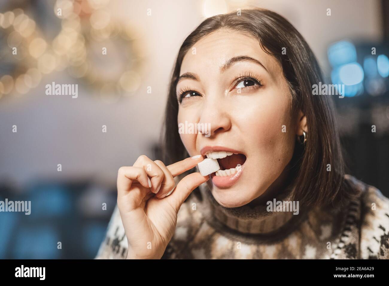 La donna asiatica ha sapori e stuzzichini un pezzo di zucchero bianco raffinato. Il concetto di consumo eccessivo di carboidrati veloci e la salute dentale Foto Stock