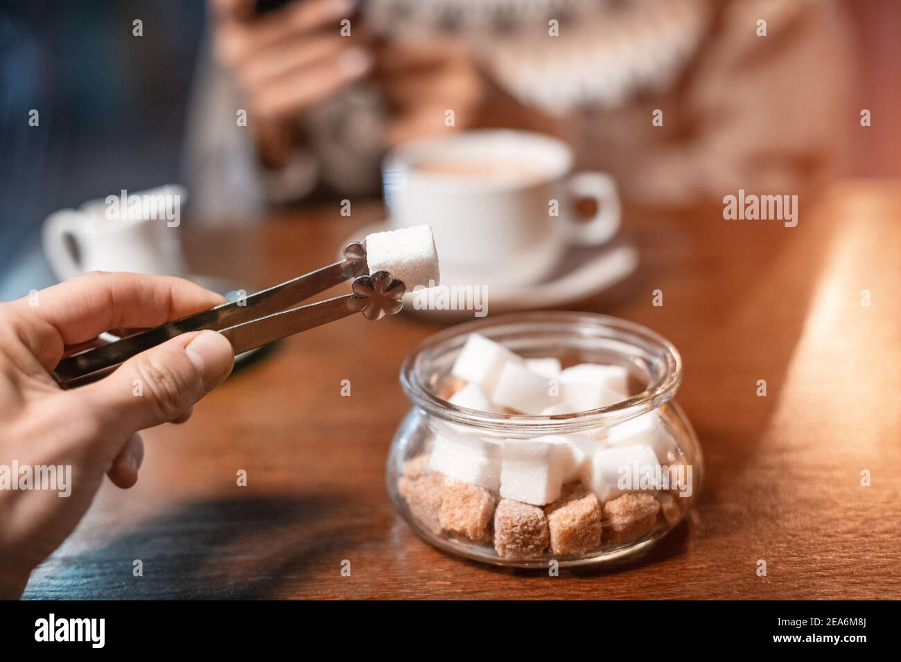Un amante del caffè addicted mette un pezzo di zucchero bianco nella sua bevanda calda nel caffè. Concetto di dieta malsana e diabete Foto Stock