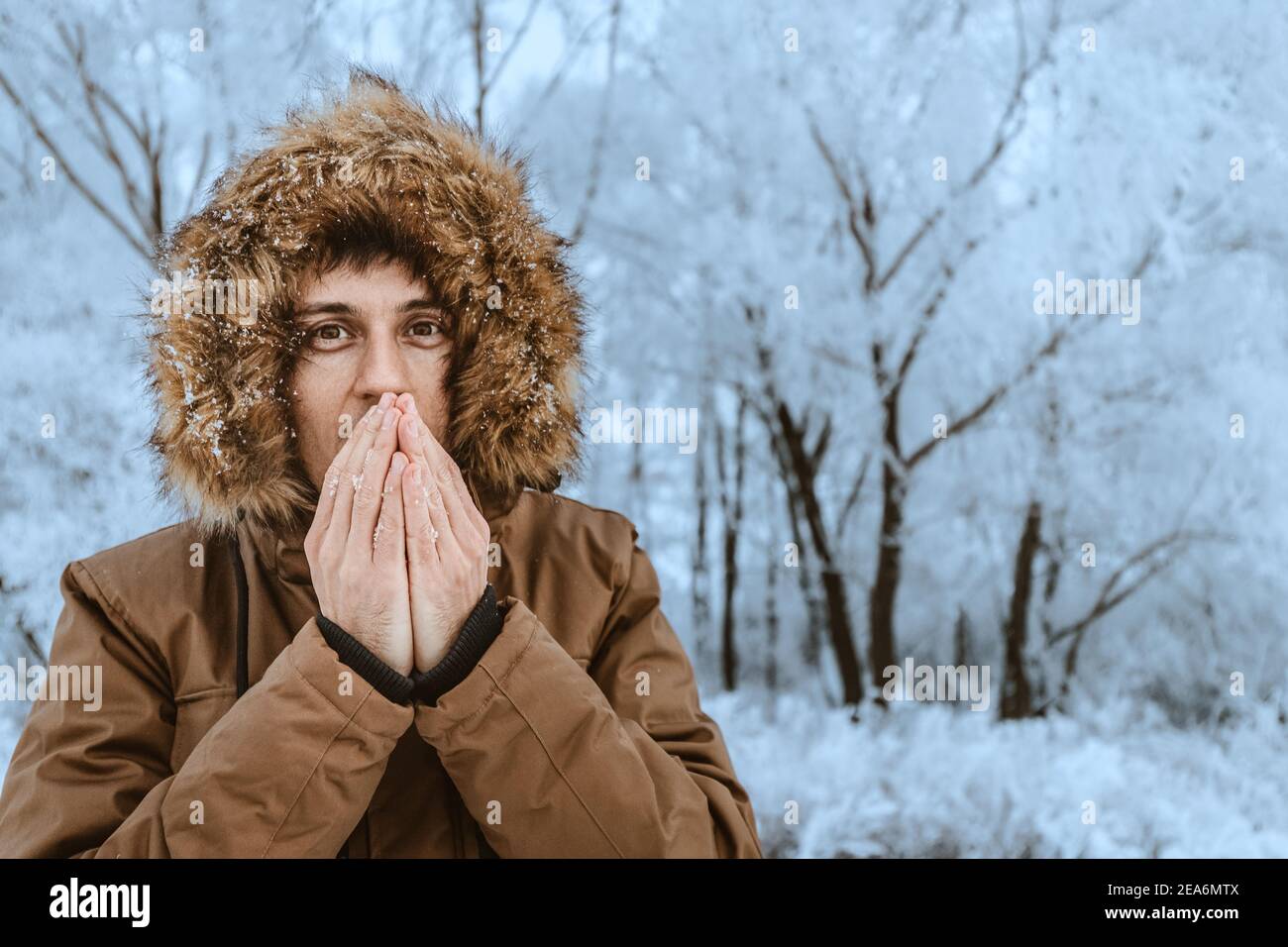 Un uomo si congela nel freddo della foresta e cerca di strofinare le mani con il respiro. Il concetto di congelamento delle estremità e ipotermia di Th Foto Stock