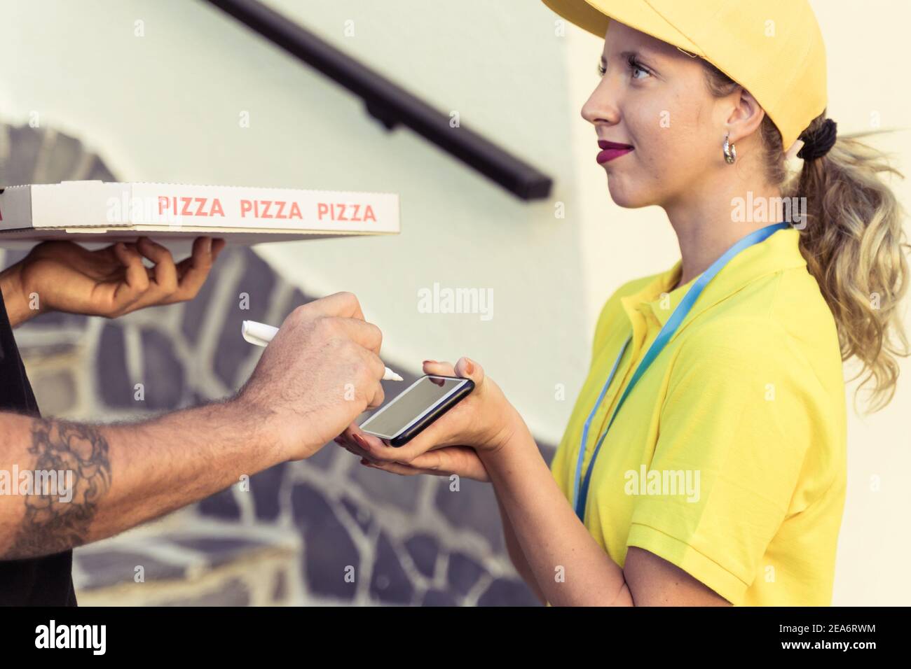 Messenger donna con uno smartphone per il pagamento. Uomo che tiene una scatola di pizza e mettere la firma per il vettore con il terminale di pagamento. Conc. Consegna pacco Foto Stock