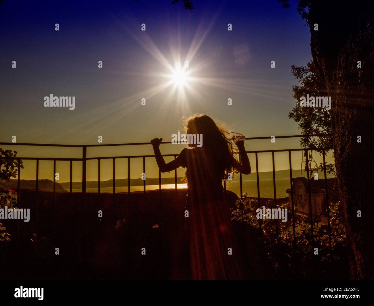 Silhouette di una ragazza che guarda una vista lago da un balcone al tramonto, Italia Foto Stock