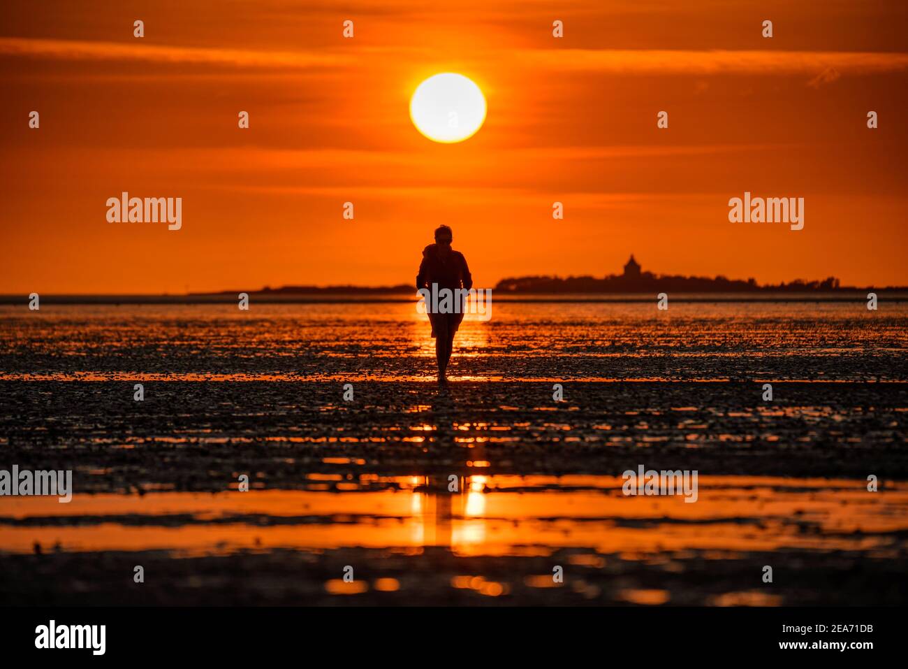 Una donna che cammina nei mudflats di Cuxhaven al tramonto Con l'isola Neuwerk sullo sfondo Foto Stock
