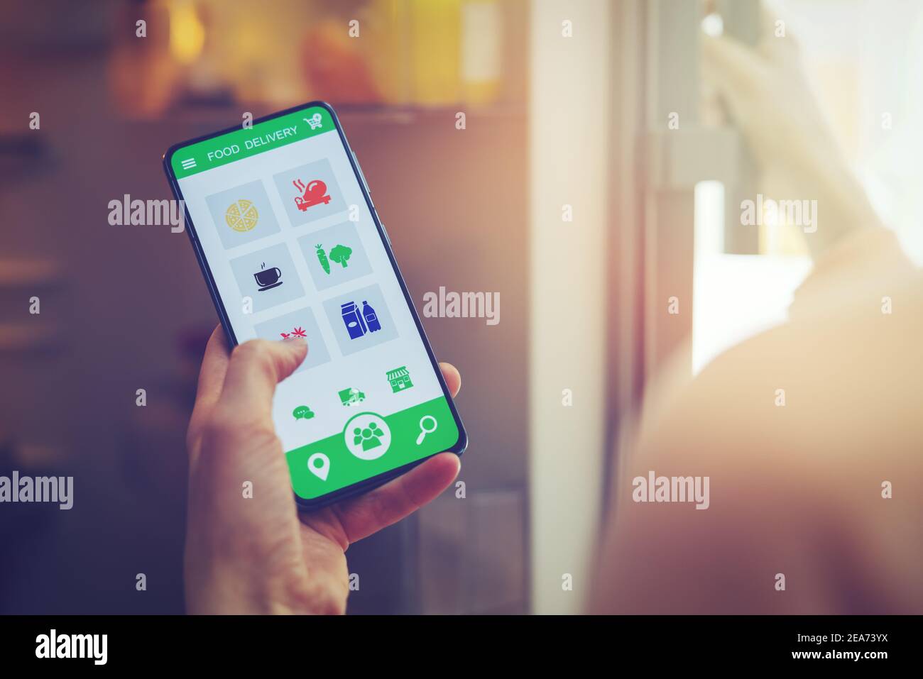 donna guarda all'interno del frigorifero e usa l'app per smartphone per ordinare la consegna di cibo Foto Stock