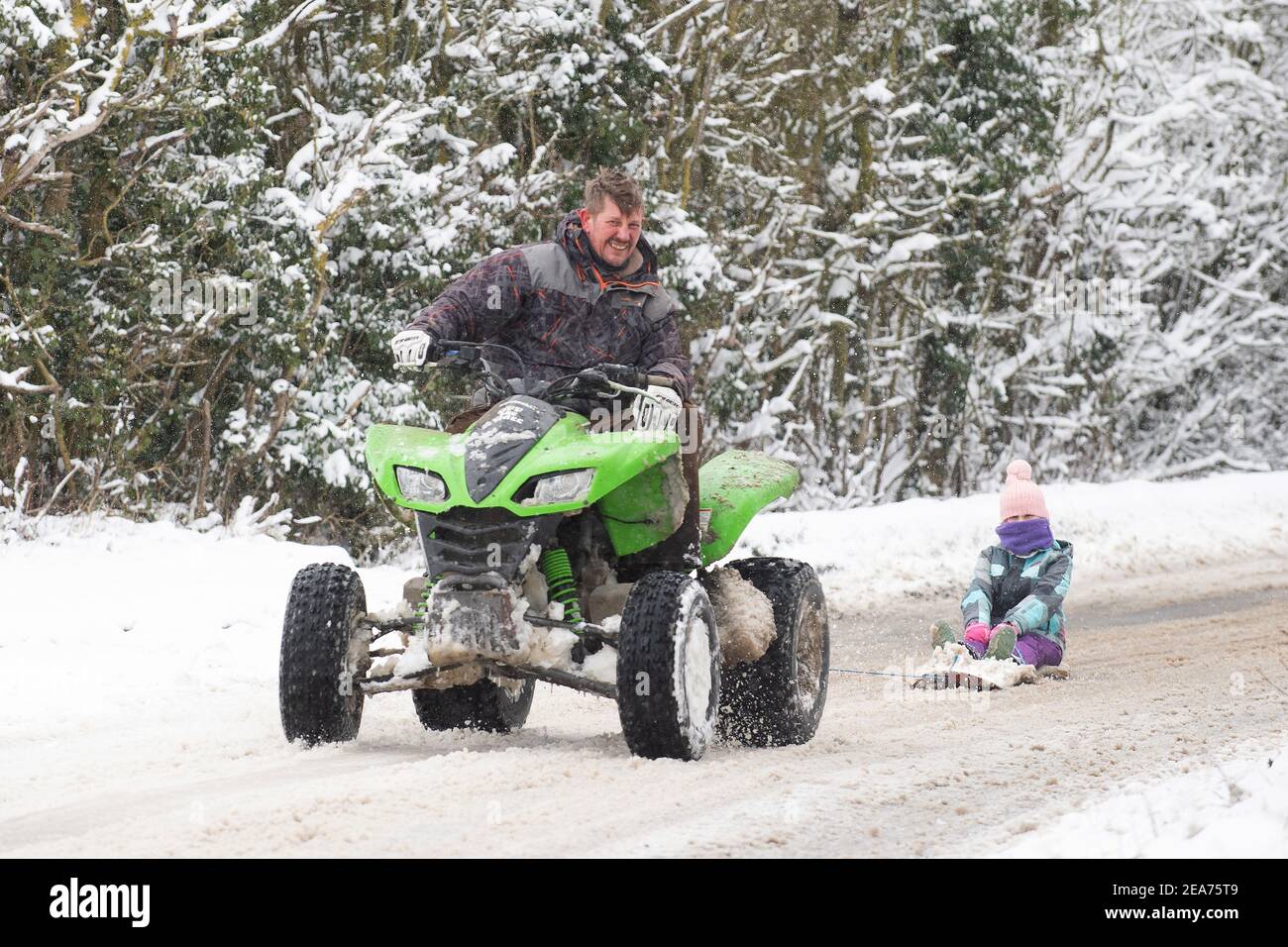 Richard Squirrel usa una moto quad per dare a sua nipote Firenze un giro nella neve a Wattisham in Suffolk, con la neve pesante impostata per portare la distruzione nel sud-est dell'Inghilterra e nell'East Anglia, mentre i venti amaramente freddi continuano a afferrare gran parte della nazione. Data immagine: Lunedì 8 febbraio 2021. Foto Stock