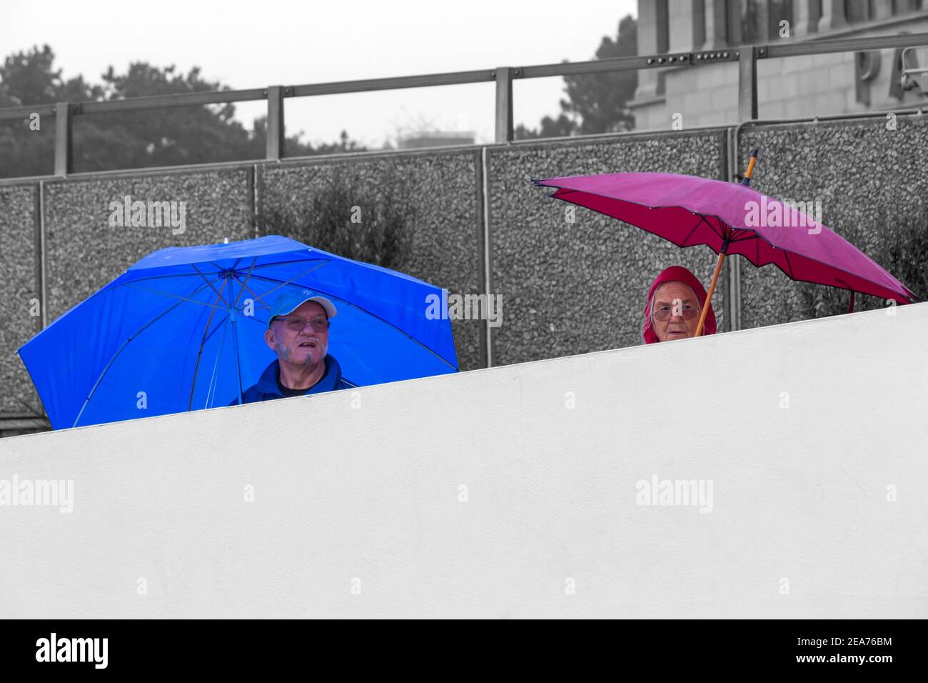 Uomo al riparo sotto ombrello blu, donna al riparo sotto ombrello rosso, sotto la pioggia a Bournemouth, Dorset UK nel mese di dicembre Foto Stock