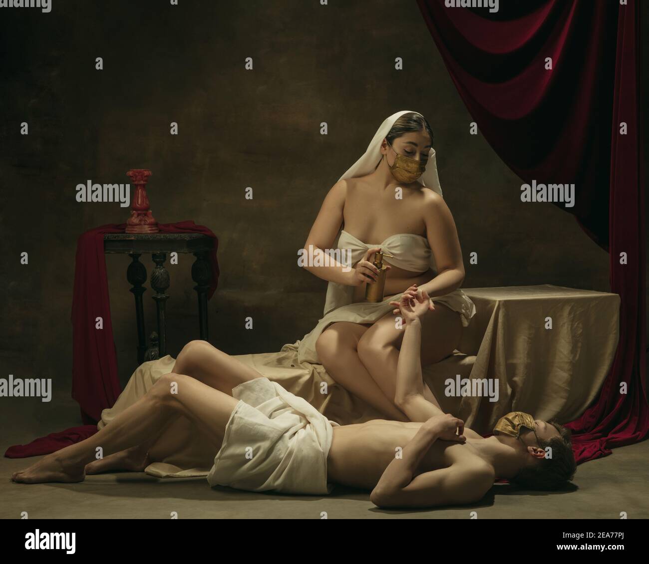 Lavate le mani con l'igienizzatore. Moderno remake di opere d'arte classiche con tema coronavirus - giovane coppia medievale su sfondo scuro, di colore dorato. Concetto di coronavirus, pandemia, creatività. Foto Stock