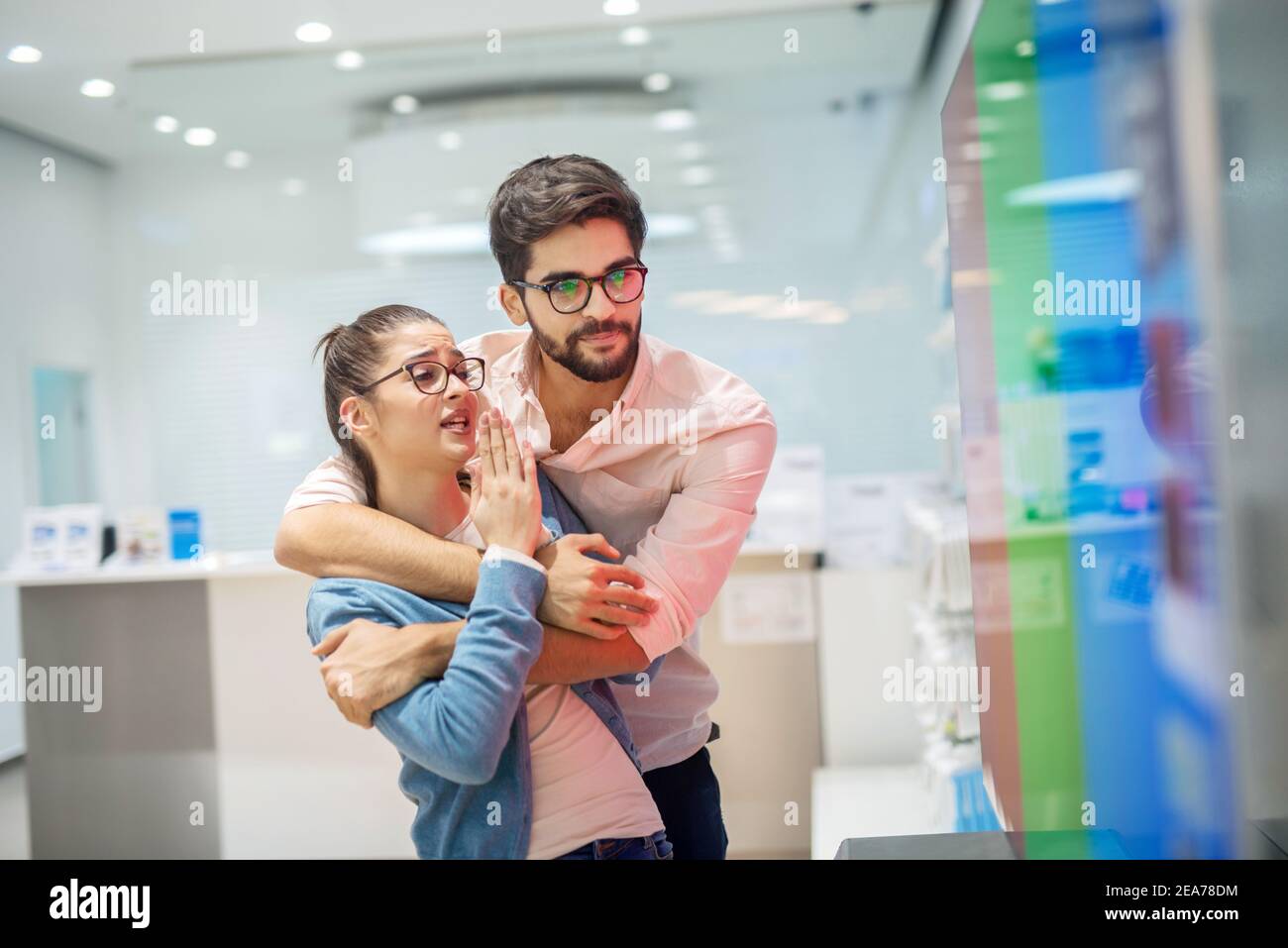 Giovane coppia allegra in negozio elettronico. Fidanzata convincendo il suo ragazzo a dalla sua nuova TV per la loro casa. Foto Stock