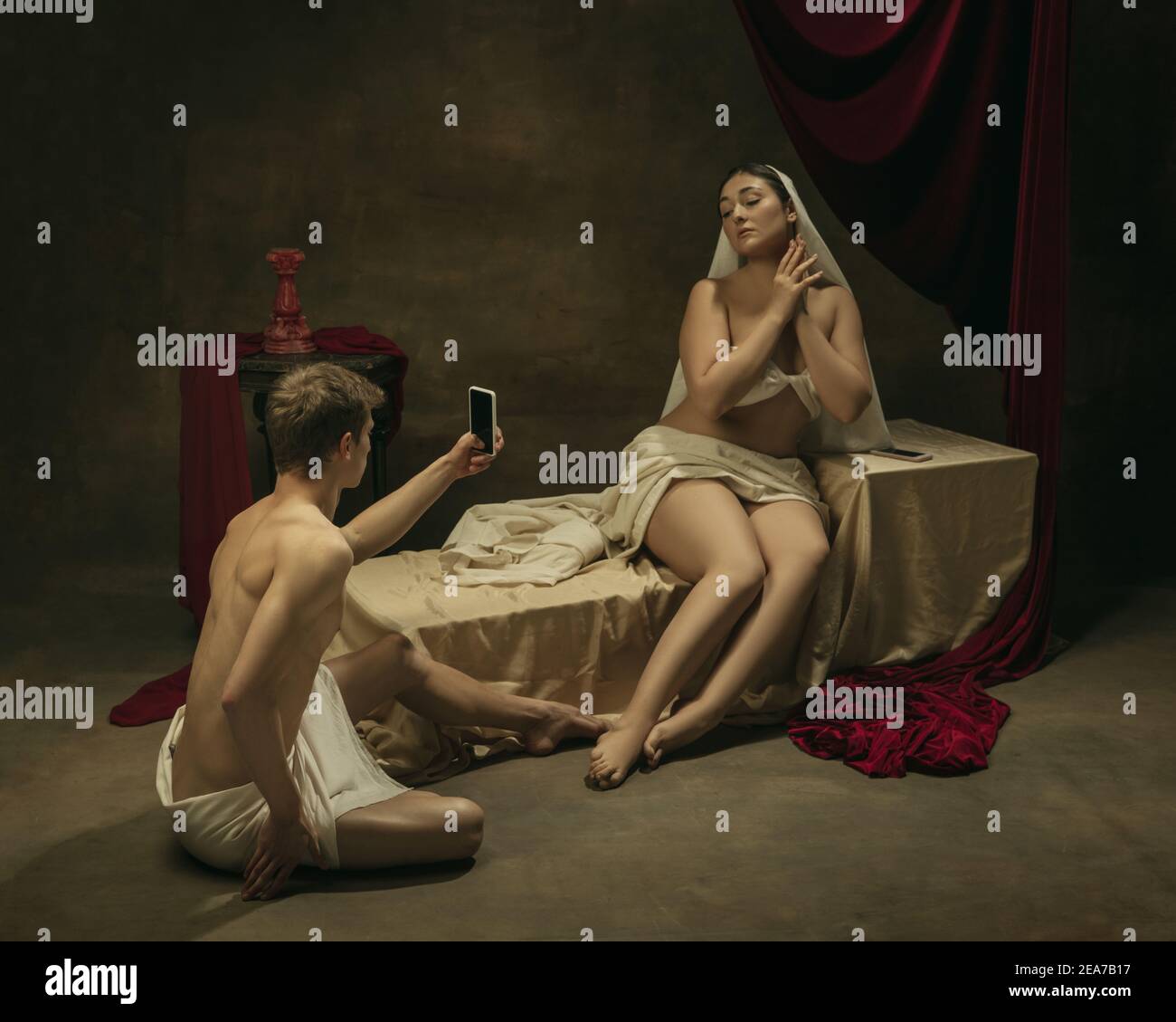 Scatta una foto per i social network. Rifacimento moderno di opere d'arte classiche a tema tecnologico moderno - giovane coppia medievale su sfondo scuro, color oro. Concetto di tecnologie, dispositivi, comunicazione, pubblicità. Foto Stock