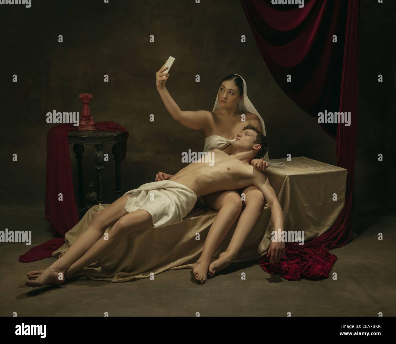 Prendi selfie per i social. Rifacimento moderno di opere d'arte classiche a tema tecnologico moderno - giovane coppia medievale su sfondo scuro, color oro. Concetto di tecnologie, dispositivi, comunicazione, pubblicità. Foto Stock