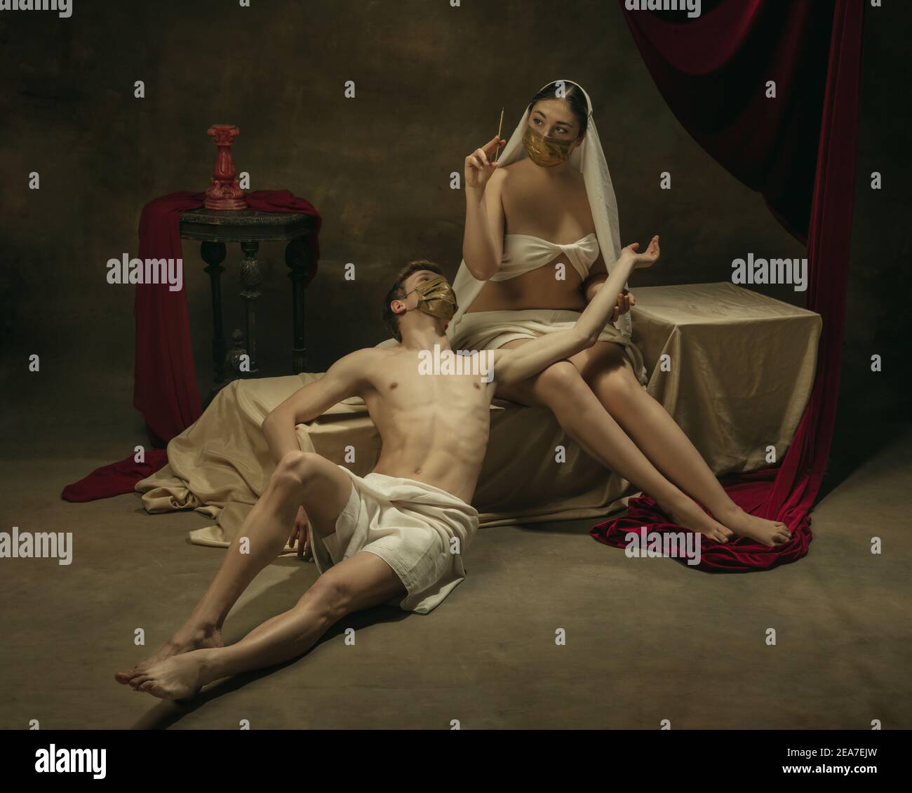 La vaccinazione sta iniziando qui. Moderno remake di opere d'arte classiche con tema coronavirus - giovane coppia medievale su sfondo scuro, di colore dorato. Concetto di coronavirus, pandemia, creatività. Foto Stock