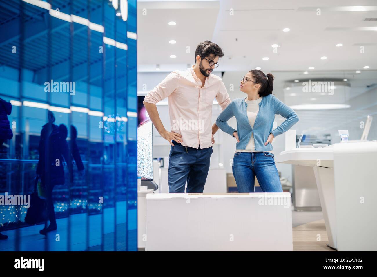 Giovane coppia in piedi e discutere di Smart TV che acquistano. Foto Stock