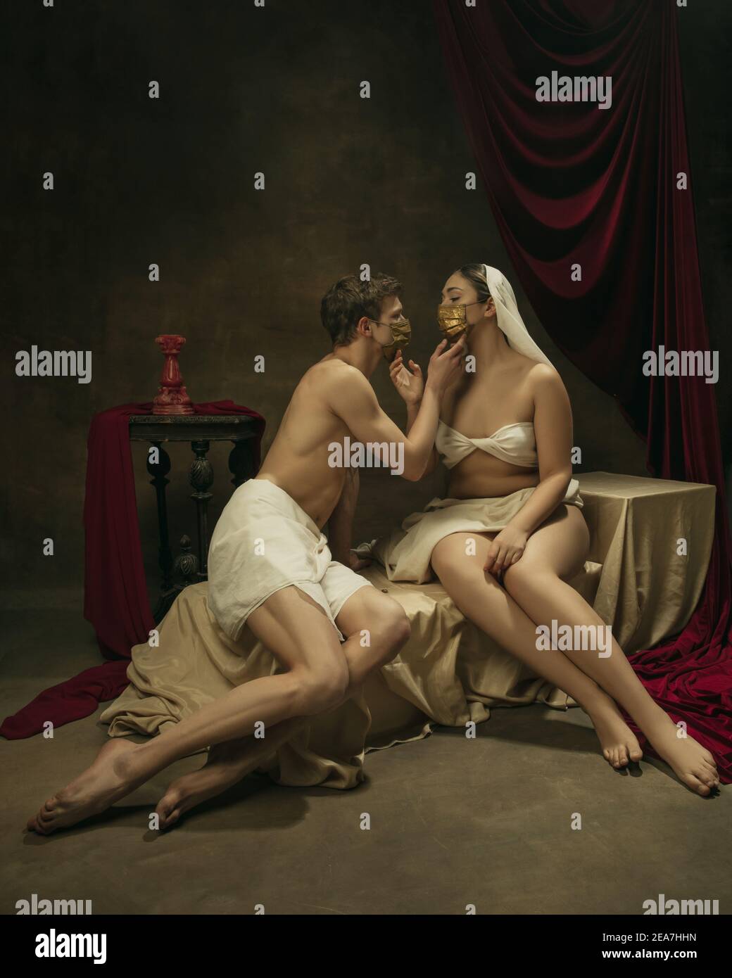 Tenerezza nei tocchi. Moderno remake di opere d'arte classiche con tema coronavirus - giovane coppia medievale in maschere di faccia su sfondo scuro, di colore dorato. Concetto di coronavirus, pandemia, creatività. Foto Stock