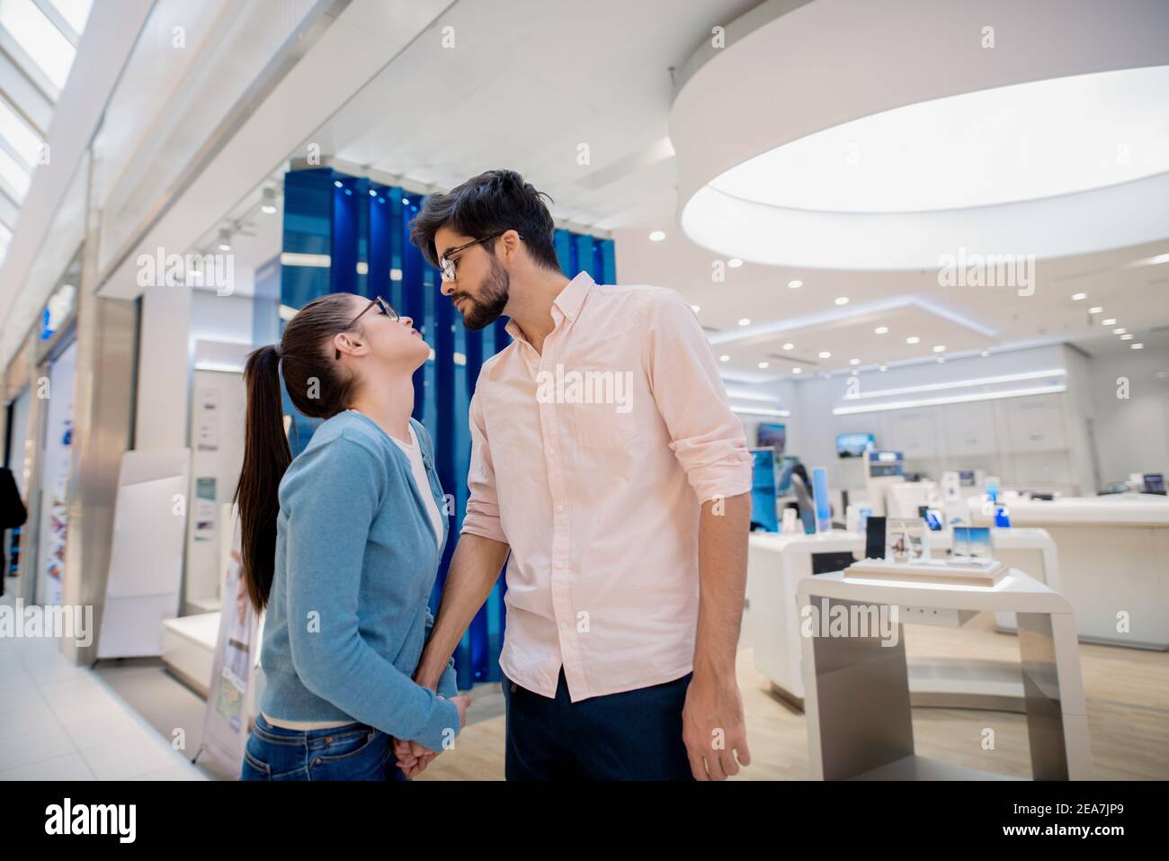 Coppia carina in piedi in negozio di tecnologia e tenendo le mani. Concetto di tecnologie New AGE. Foto Stock