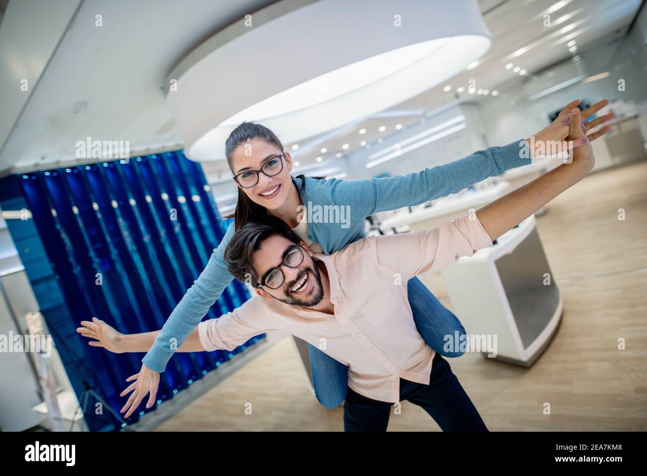 Felice giovane coppia caucasica che ha piggyback in negozio di tecnologia. Concetto di nuove tecnologie. Foto Stock