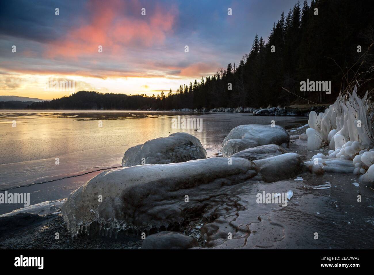 Riva ghiacciata del lago al tramonto. Lago Jonsvatnet vicino Trondheim in Norvegia. Splendidi colori del tramonto sul cielo e le nuvole. Modelli di ghiaccio e. Foto Stock