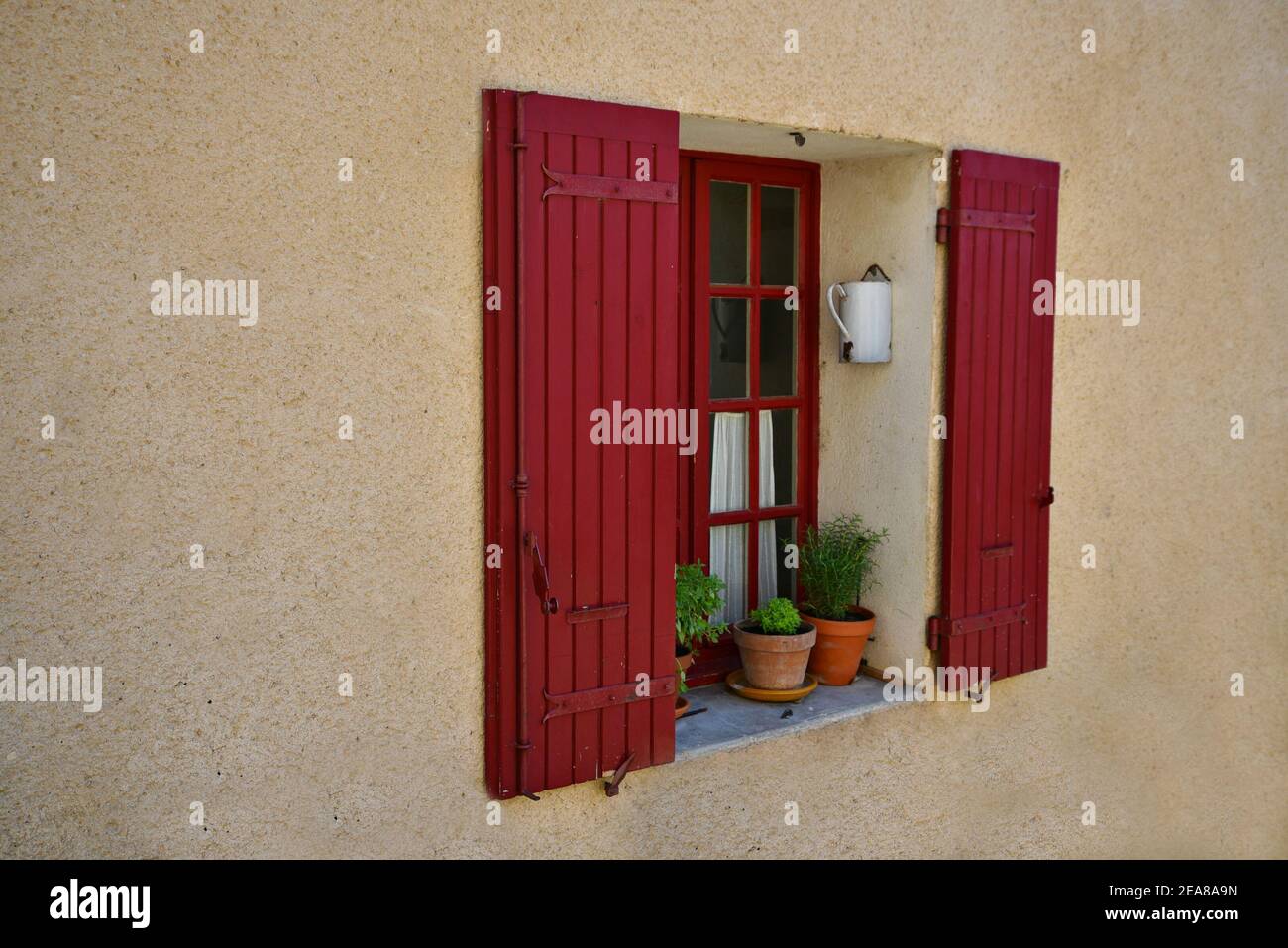 Tradizionale rustico finestra in legno rosso con persiane e vasi di argilla con fiori su un muro di gesso ocra a Venasque, Vaucluse Provence, Francia. Foto Stock
