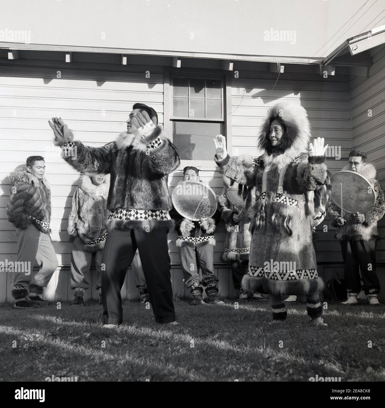 1960, storico, al confine esterno di Anchorage, Alaska, USA, al di fuori di un edificio di legno a un piano, i nativi in abito tradizionale di pelli animali e pellicce esecuzione di una danza. L'Alaska divenne il 49° stato degli Stati Uniti nel 1959, ma fu occupata da diverse popolazioni indigene per migliaia di anni prima dell'arrivo degli europei. Dato che lo Stato ha un confine marittimo con la Russia, sono stati loro a stabilirsi per primi, stabilendo ciò che è diventato noto come America russa. Le popolazioni indigene costituiscono oltre il 15% della popolazione e i nativi dell'Alaska svolgono un ruolo importante nel governo locale Foto Stock