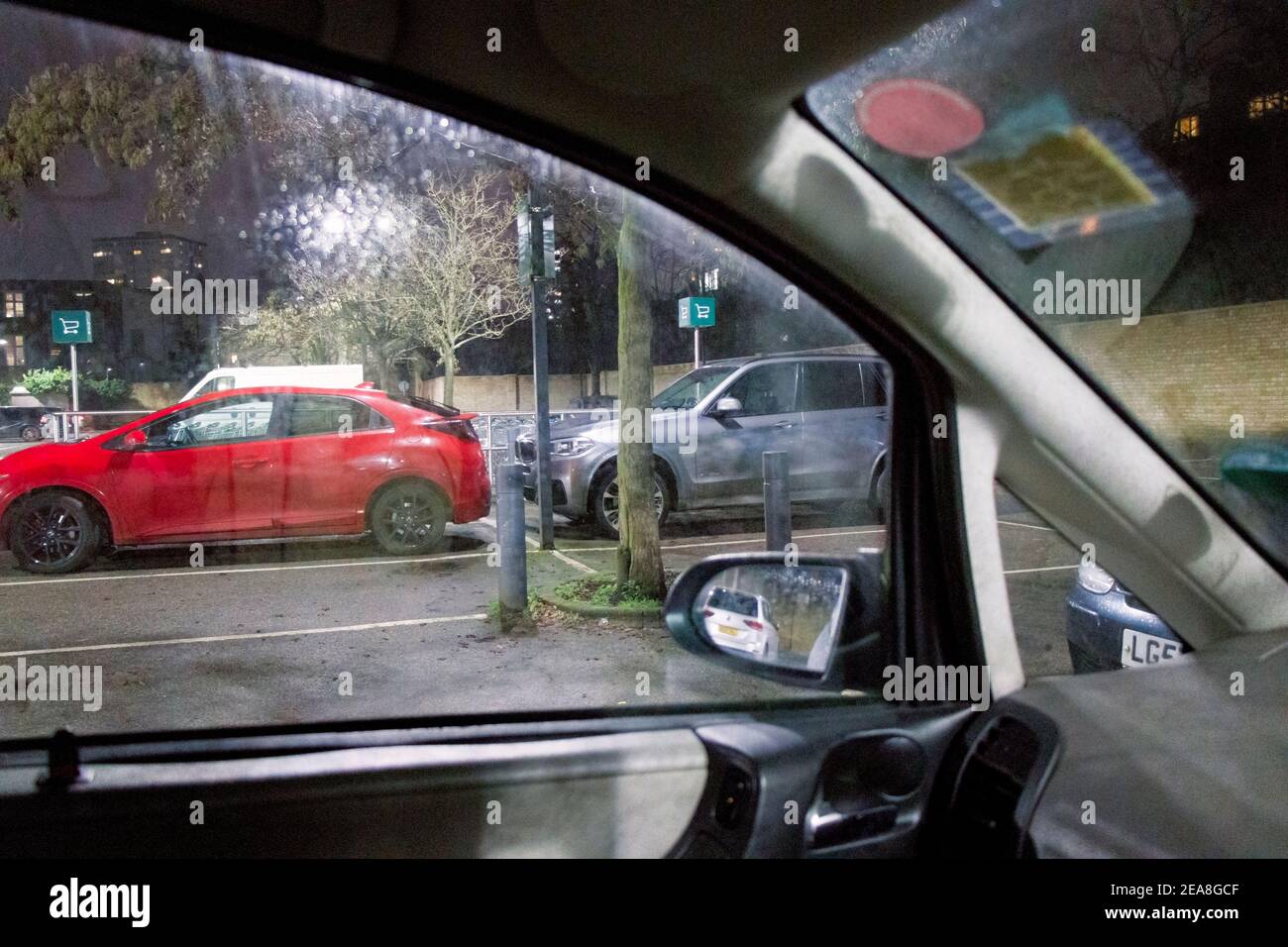 Vista attraverso la finestra laterale di un'auto parcheggiata durante una noiosa attesa in un parcheggio supermercato in una fredda serata invernale sotto la pioggia, Londra, Regno Unito Foto Stock