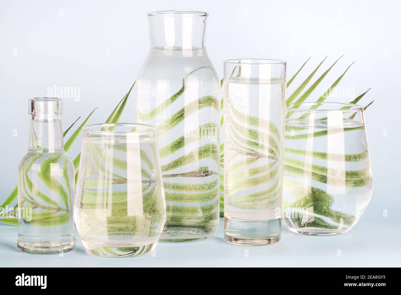 foglia di palma distorta attraverso l'acqua in bicchieri e bottiglie su sfondo blu. Arredamento domestico, eco-friendly, acqua pura, giardinaggio concept.natura sfondo Foto Stock