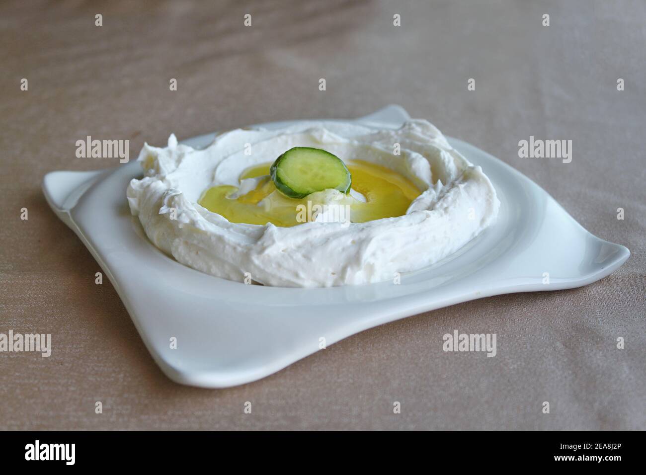 Un piatto di labneh fresco con olio d'oliva e un cetriolo. Foto Stock
