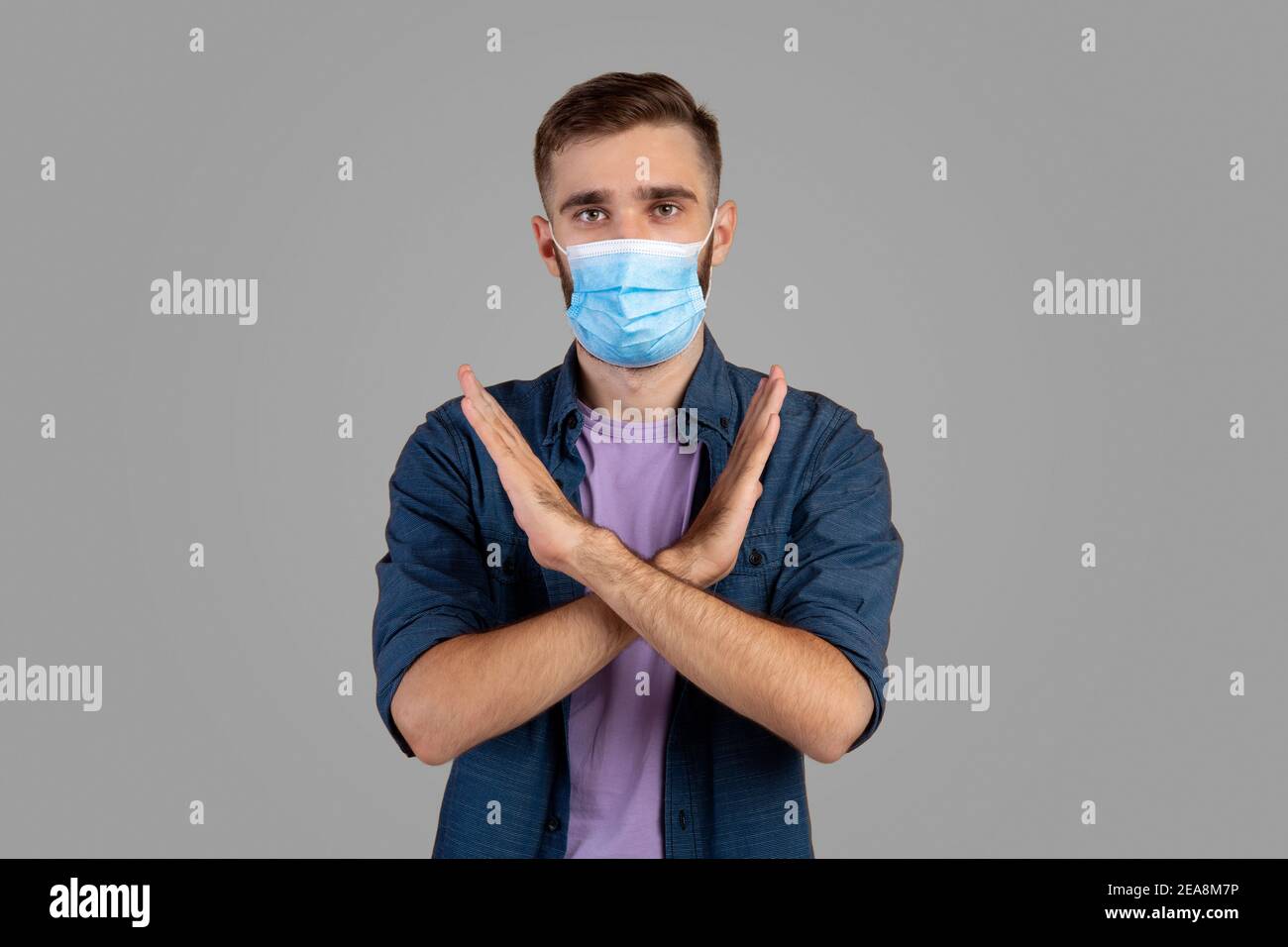 Lotta al coronavirus. Serio uomo caucasico in maschera di faccia gesturing STOP su sfondo grigio studio Foto Stock