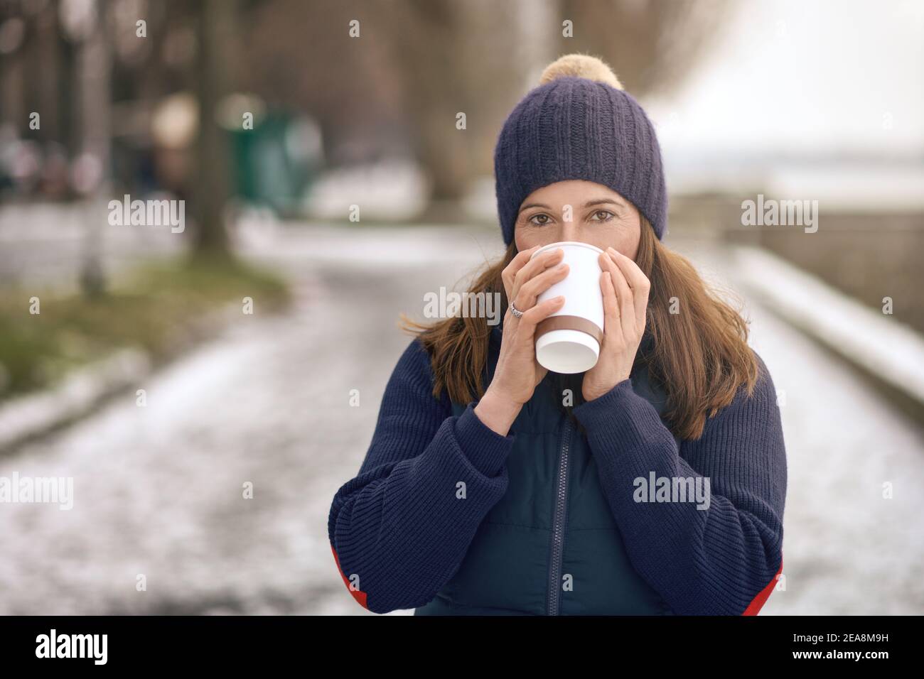 Donna bruna felice di mezza età che va per una passeggiata e bere un caffè da andare Foto Stock