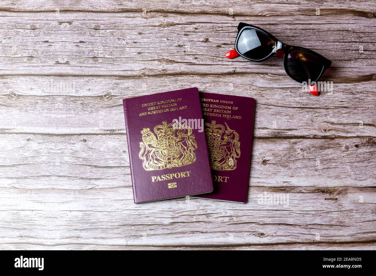 Un paio di passaporti britannici posati su un tavolo di legno accanto a un paio di occhiali da sole Foto Stock