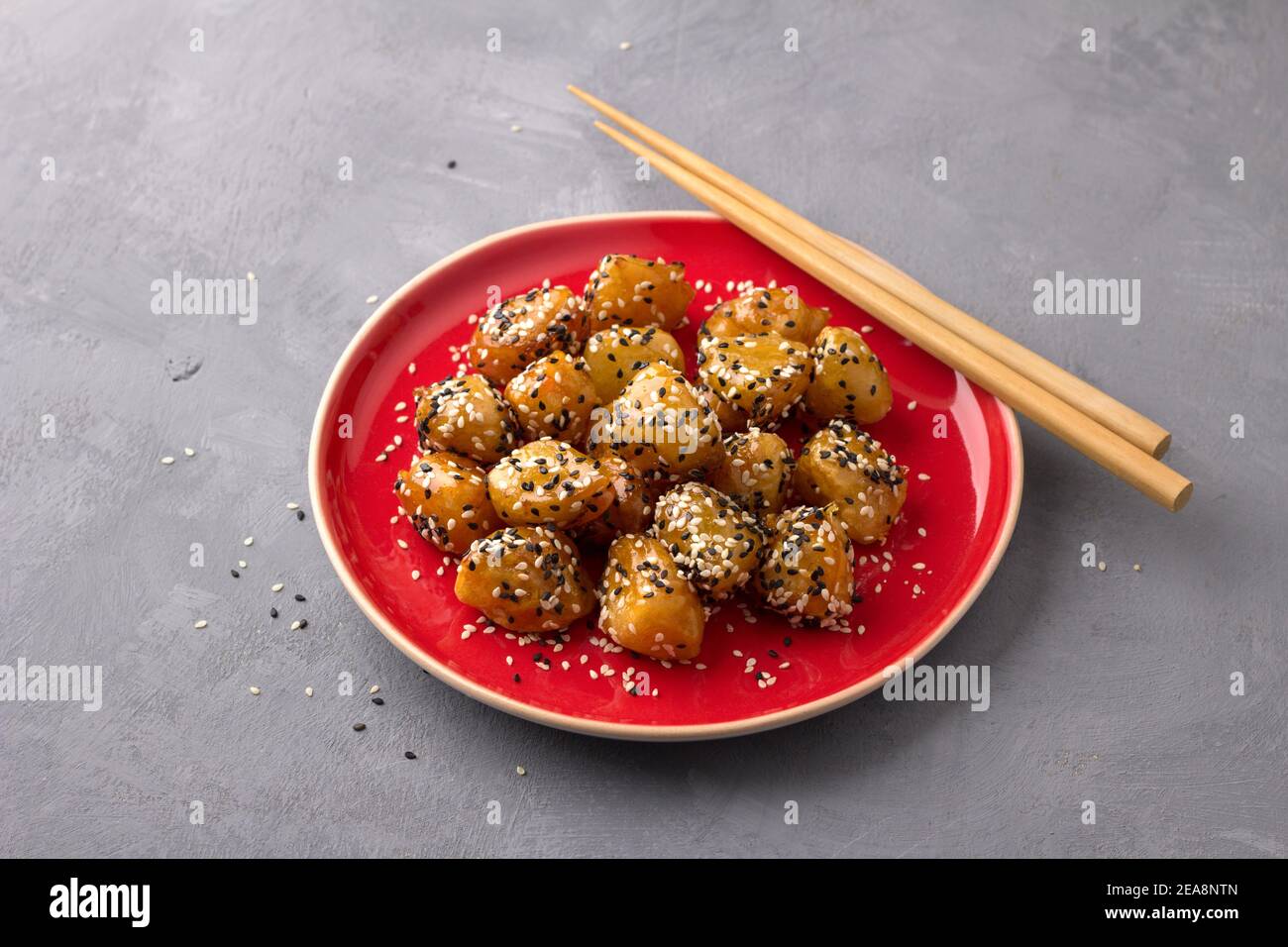 Mele tradizionali fritte сhinese in caramello con semi di sesamo piatto rosso vintage con chopsticks su sfondo grigio testurizzato Foto Stock